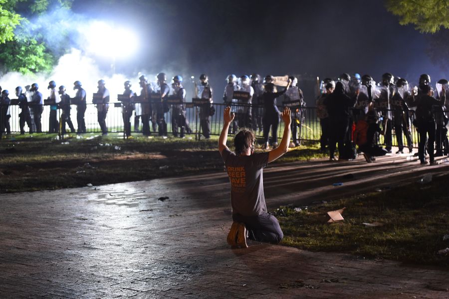 A protester kneels and holds up his hands in front of a row of police during a demonstration near the White House. (Photo by ROBERTO SCHMIDT/AFP via Getty Images)