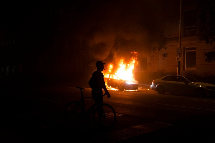 A demonstrator watches a car burn near the White House in Washington. (AP Photo/Evan Vucci)